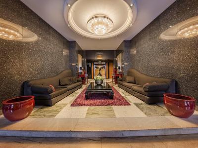 Elegante hotel lounge met kroonluchter, banken, tapijt en decoratieve rode vazen.