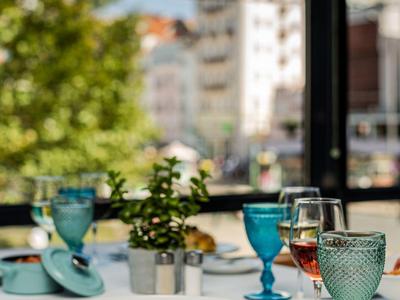 Een gedekte tafel met kleurrijke glazen en een gedecoreerd bord voor een raam met uitzicht op de stad.