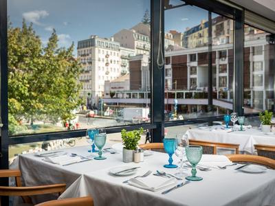 Licht gedekte tafel met kleurrijke glazen en stadszicht door grote ramen in een restaurant.