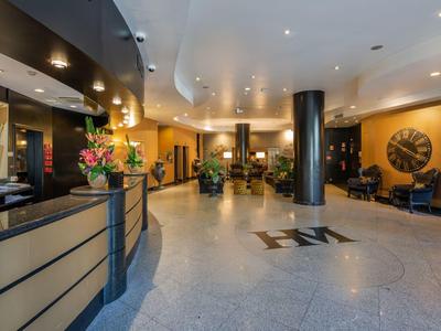 Ruime hotel lobby met receptiebalie, zitgedeeltes en moderne verlichting.