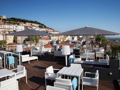 Dachterrasse mit weißen Möbeln, Sonnenschirm und Blick auf die Stadt bei klarem Himmel.
