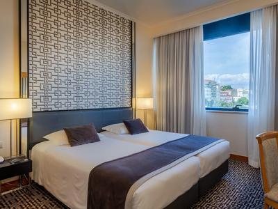 Modern hotelkamer met tweepersoonsbed, nachtlampjes en uitzicht op de stad via raam.