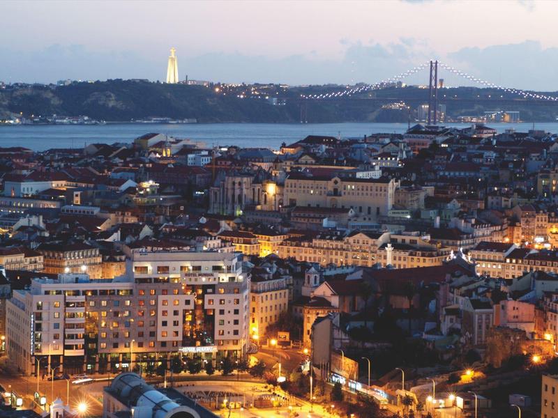 Uitzicht over een verlichte stad met rivier, brug en heuvels op de achtergrond bij schemering