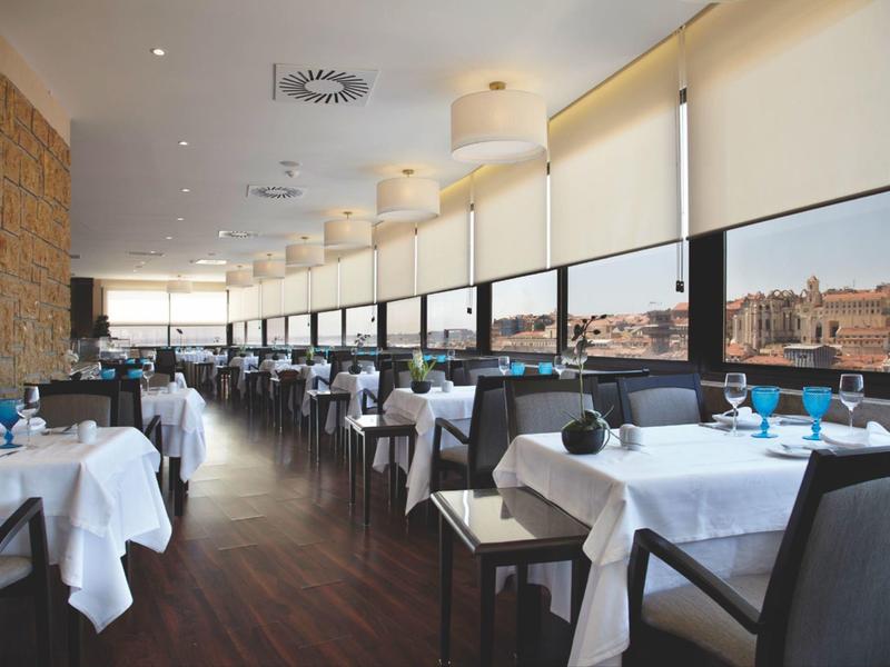 Modern restaurant met witte tafelkleden en panoramische ramen met uitzicht op de stad.