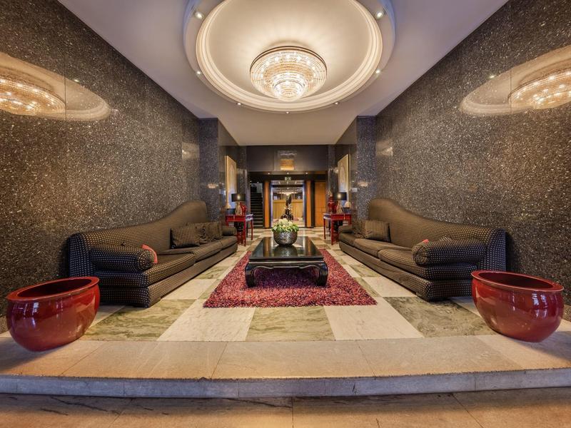 Elegante hotel lounge met kroonluchter, banken, tapijt en decoratieve rode vazen.