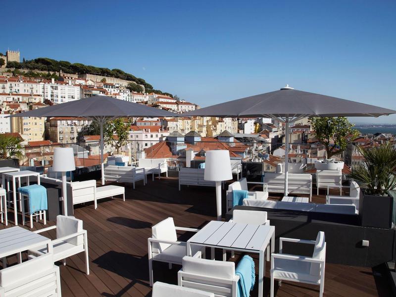 Moderne dakterras met witte zitmeubels en grote parasol met uitzicht op stad en heuvels.