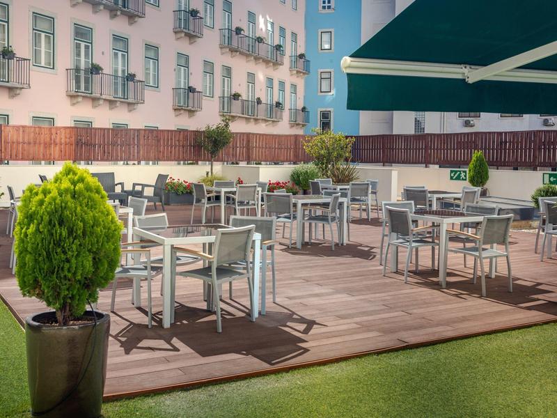 Leeg buitengebied van een hotel met tafels, stoelen en planten op een houten terras.