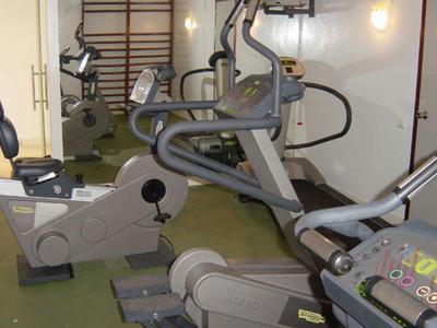 Fitnessraum mit mehreren Trainingsgeräten und Spiegel an der Wand.