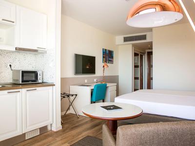 Světý hotelový pokoj s kuchyňským koutem, psacím stolem, manželskou postelí a moderním vybavením.