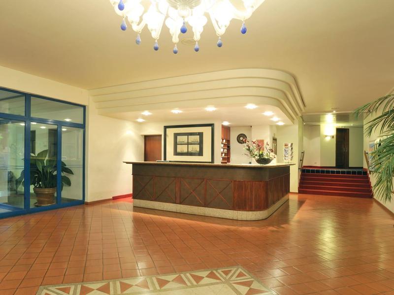 Recepce v elegantním hotelu s velkými vstupními dveřmi a rostlinami.