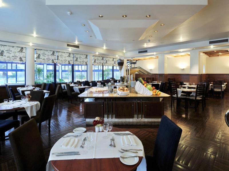 Elegantní restaurace s prostřenými stoly, moderním zařízením, velkými okny a tmavou dřevěnou podlahou.