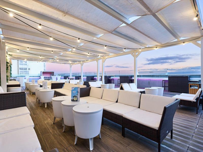 Terraza en la azotea moderna con muebles lounge blancos y luces al atardecer.