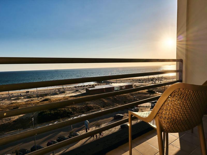 Balcón con silla y vista al mar al atardecer en una habitación de hotel.