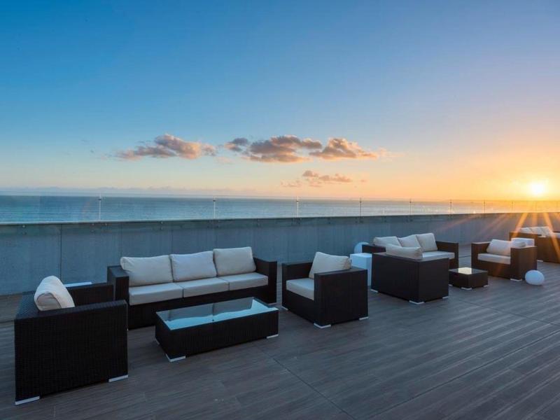 Conjunto de asientos modernos en terraza de hotel con vista al mar al atardecer.