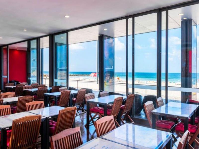 Comedor moderno con sillas de madera y vista a la playa a través de grandes ventanales.