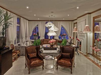 Elegantes Wohnzimmer mit antiken Möbeln, Stehlampen und großer Fensterfront bei Abendlicht.