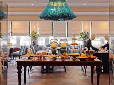 Un buffet con succhi freschi, panini e frutta in un ristorante luminoso con grandi finestre.