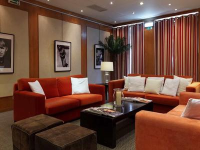 Gemütliches Wohnzimmer mit roten Sofas, dunklem Holztisch, Lampen und modernen schwarz-weißen Bildern.