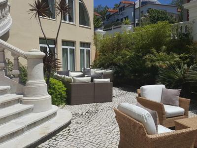 Area esterna con pavimento in ciottoli, mobili in vimini e piante accanto alle scale.