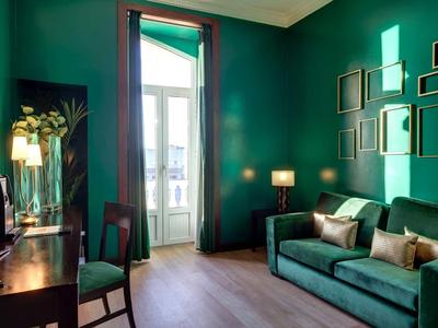 Camera d'hotel accogliente con parete verde, divano, scrivania e vista sul balcone.