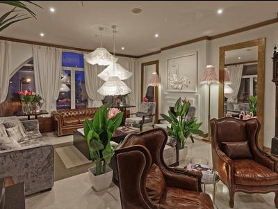 Elegante salotto d'hotel con poltrone in pelle, grandi piante e orologio a pendolo classico.