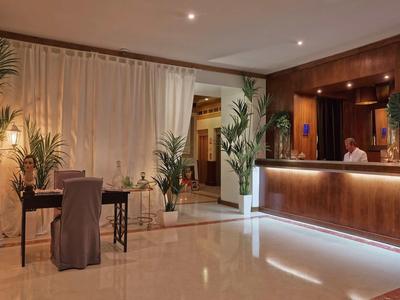 Elegante hall dell'hotel con reception illuminata, area salotto e piante.