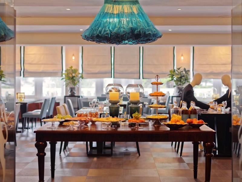 Un buffet con succhi freschi, panini e frutta in un ristorante luminoso con grandi finestre.