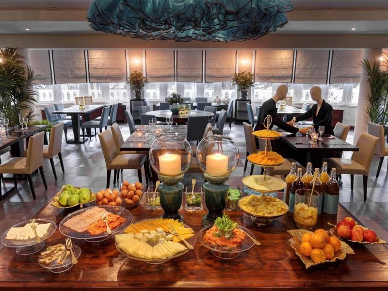 Buffet con vari piatti in un elegante ristorante con tavoli apparecchiati sullo sfondo.