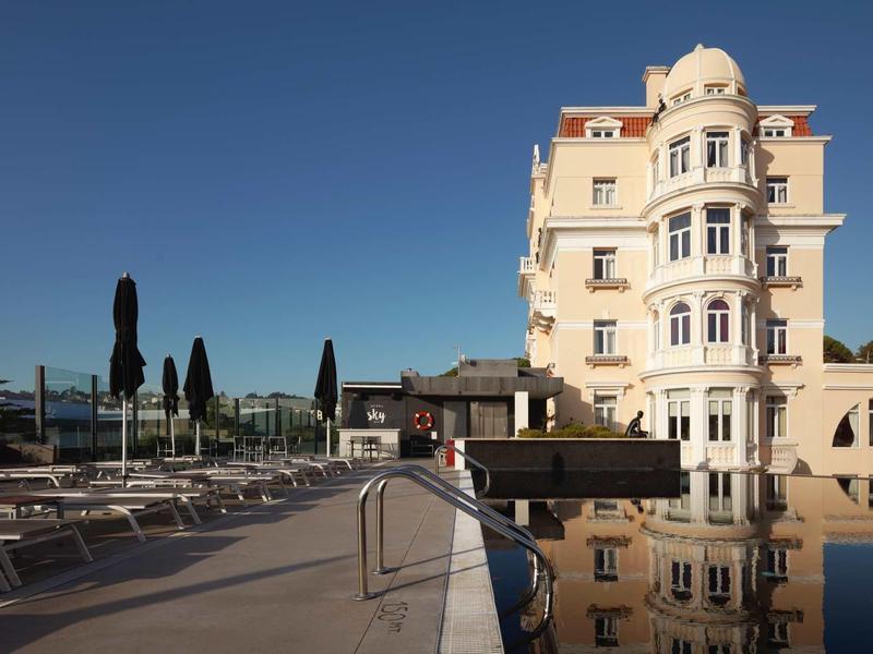 Hotel elegante con terrazza solarium e piscina all'aperto sotto un cielo azzurro.