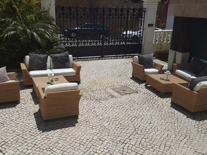 Area esterna con mobili imbottiti su pavimentazione acciottolata davanti a una recinzione.