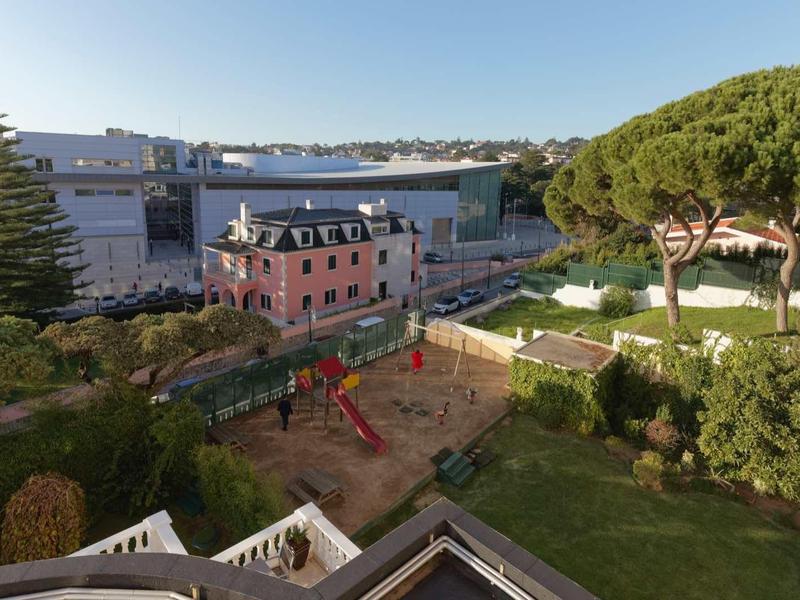 Vista di un'area giochi accanto a un edificio rosa e alberi in una zona alberghiera.