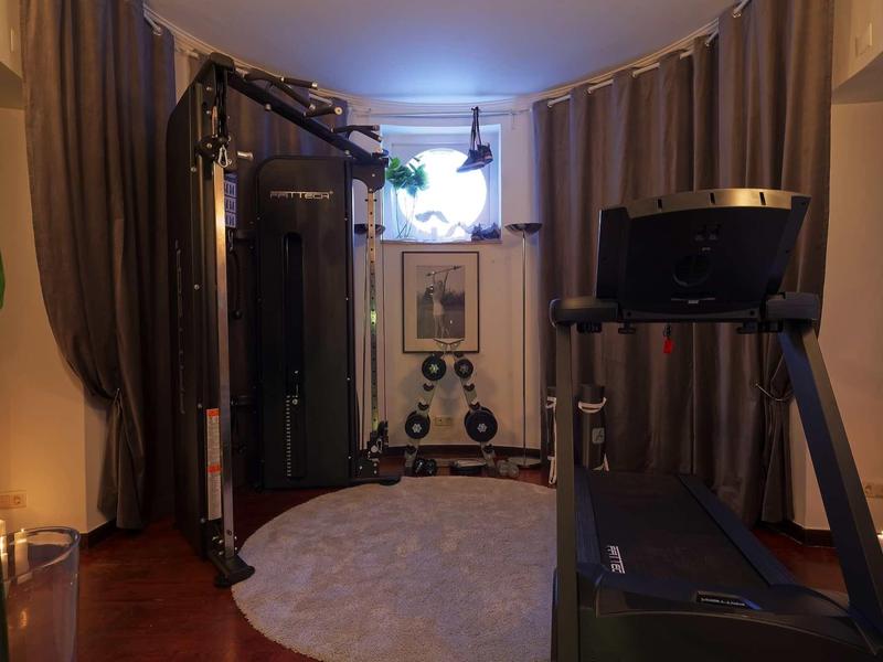 Piccola palestra con macchina per forza, tapis roulant, specchio e tappeto rotondo.