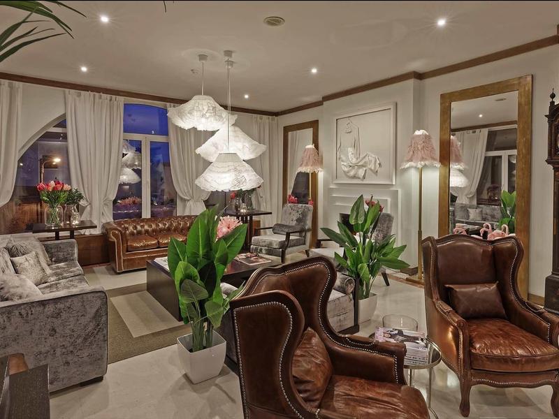 Elegante salotto d'hotel con poltrone in pelle, grandi piante e orologio a pendolo classico.