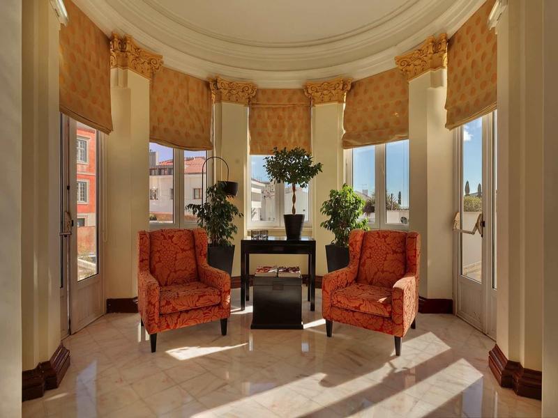 Elegante area salotto con due poltrone rosse e piante davanti a grandi finestre di una camera d'hotel.