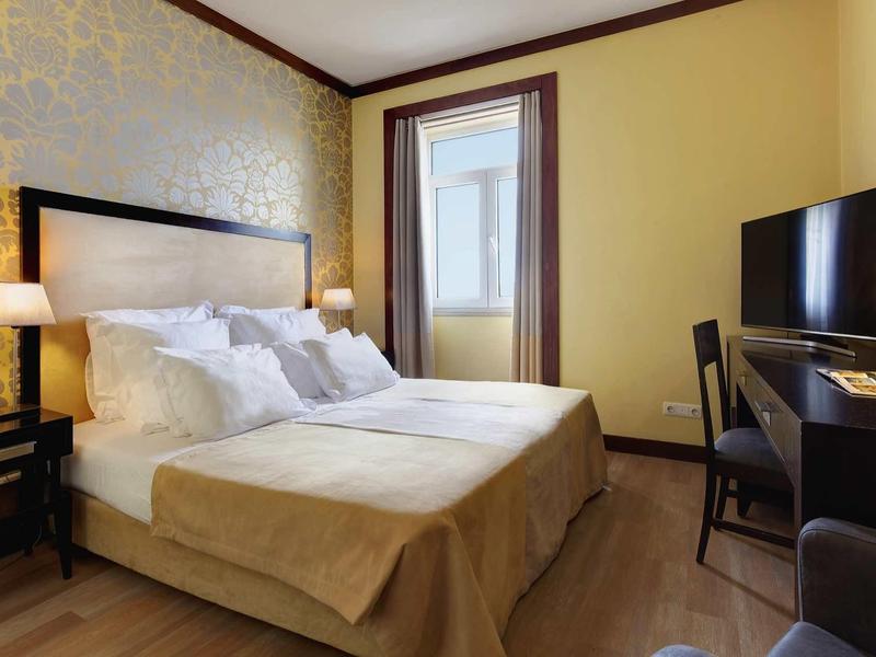 Camera d'hotel accogliente con letto matrimoniale, lampade da comodino e scrivania con TV.