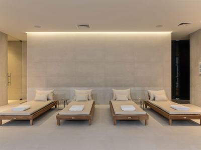 Modern lounge area with four wooden benches and beige cushions against a lit wall.