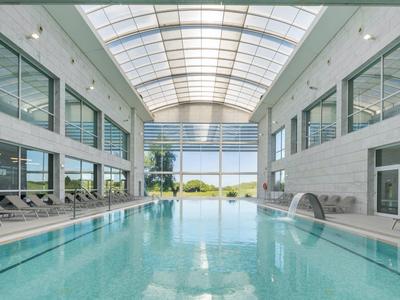 Indoor pool in a modern hotel with glass roof and lounge chairs by the poolside.