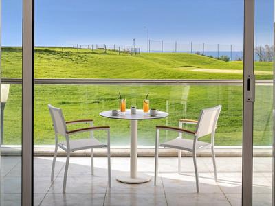 Balcony table with two chairs and drinks overlooking green golf course grounds.