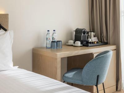 Modern hotel room area with desk, coffee machine, water bottles, and blue chair.