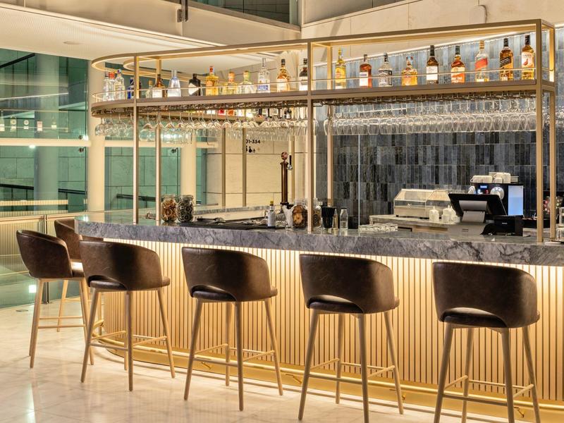 Modern hotel bar area with tall bar stools and shelves filled with spirits.