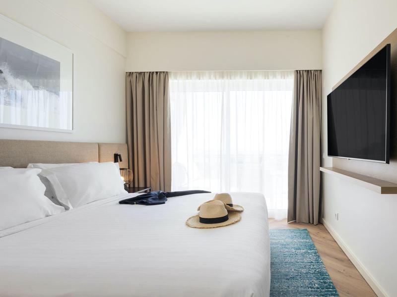 Modern lounge area with four wooden benches and beige cushions against a lit wall.