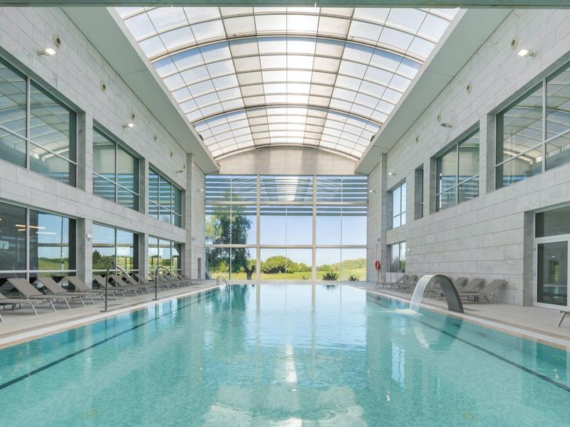 Indoor pool in a modern hotel with glass roof and lounge chairs by the poolside.