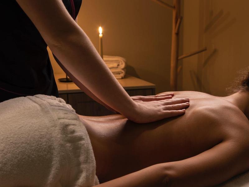 Person receiving a relaxing back massage in a warmly lit room with a burning candle.