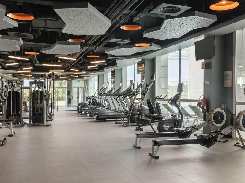 Modern gym with treadmills, rowing machines, and weight equipment in a bright space.