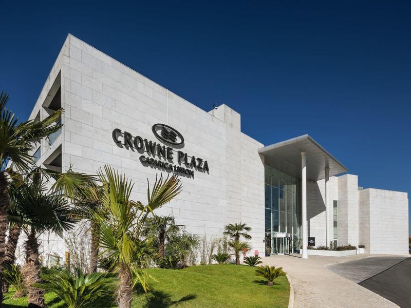 Modern white hotel entrance with clear Crowne Plaza signage and palm trees