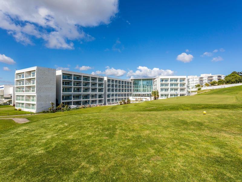 Modern hotel building with large windows in front of a green lawn under a blue sky.