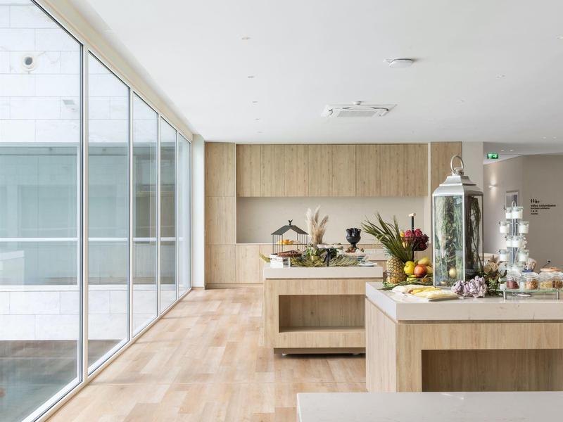 Bright, modern breakfast buffet in a room with large glass wall and wooden floor.