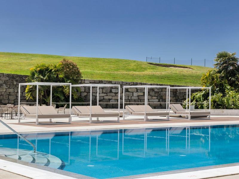 Modern pool area with loungers and green lawn in the background under clear sky.