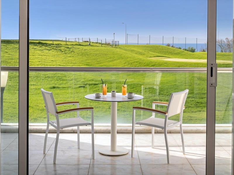 Balcony table with two chairs and drinks overlooking green golf course grounds.