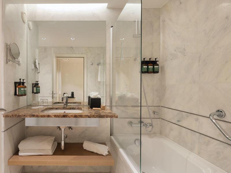 Modern bathroom with marble walls, sink, mirror, and bathtub with shower divider.